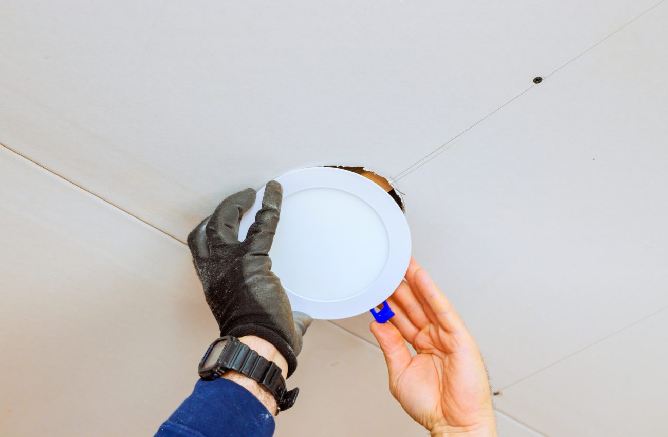 Worker installs a recessed light fixture in a ceiling during a home renovation project in daylight